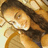 Pixelated image of a person with long dark hair wearing an orange top, smiling while holding something near their face.
