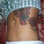 A pixelated image of a person's torso with visible tattoos, wearing a white collar and red patterned fabric background.