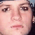 Pixelated close-up of a person's face with light skin tone, dark eyes, and a neutral mouth expression against a blurred background.