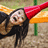 A pixelated image of a person with long dark hair wearing a red headband, lying on a sandy surface near an orange and green structure.