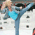 Pixelated figure in blue pants and black shoes performs a high kick, holding a light blue heart-shaped object against a white background with scattered dark squares.