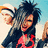 Pixelated image of two people with spiky hair, one in red and black clothing, the other in white and orange, with a black text logo on the right.