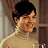 Static pixelated image of a person with short dark hair wearing a light-colored turtleneck sweater against a blurred indoor background.