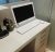 Pixelated image of a white desk with a black monitor, dark chair, and light-colored wall background.