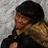 Pixelated image of a person with dark hair wearing a black top and brown patterned scarf against a light gray background.
