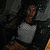 Pixelated static image of a person with dark hair wearing a light gray shirt against a dark background.