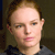 Pixelated close-up of a person with light brown hair, fair skin, and a neutral expression wearing a dark blue garment with a light gray collar.