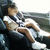 A person in a white shirt and dark shorts sits on a dark couch with legs crossed, wearing white shoes.