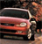 A static pixelated image of a red vehicle with a person standing beside it, viewed from a low angle.