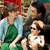 Static 50x50 pixel icon showing two figures in close proximity with one figure holding a small object, rendered in low-resolution pixel art style with visible dithering and color blending.
