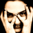 Static pixelated image of a person's face with hands near the head, featuring brown hair and dark glasses on a black background.