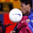 Pixelated static icon showing a person in red and pink clothing holding a white circular object with blue markings against a blurred background of yellow, brown, and blue tones.