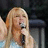 Pixelated image of a person with long blonde hair holding a microphone, set against bright cyan background with text and emoticons.