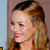 Pixelated close-up of a person with light brown hair, red lips, and a small blue earring, set against a light blue and brown background.