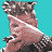 Pixelated image of a person with light brown hair and pinkish skin holding a black object against a teal background, next to a stylized black 'J' symbol.