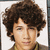 Pixelated portrait of a person with voluminous curly brown hair, light skin tone, and neutral expression against plain white background.