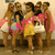 Group of five women in coordinated outfits posing together, with one woman in yellow shorts and pink top at center, others in white and blue attire.