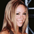Pixelated close-up of a smiling person with long light brown hair against a dark background with metallic elements.