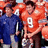 A pixelated group photo of people in sports uniforms with one person wearing a red jersey with the number 9, set against an orange background with blue text elements.