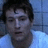 Pixelated static image of a person with dark hair and light skin wearing a white shirt against a blue background.