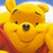 Pixelated close-up of a yellow bear with brown eyes and nose, wearing red clothing against a blue sky background.
