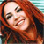 A pixelated close-up of a person with long red hair smiling, showing teeth, against a striped background.