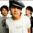 Three pixelated figures in white and dark clothing stand side-by-side against a light background, with the central figure wearing a black cap.