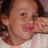 Pixelated close-up of a person with brown hair wearing a light-colored top, holding a hand near the face with visible pink and red nail polish.