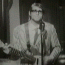 Black-and-white of nine identical frames showing a person with glasses, striped shirt, and guitar, standing before a microphone