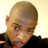 Static 48x48 pixel icon showing a close-up of a bald person with light skin wearing dark clothing and red accents, rendered in low-resolution pixel art style against a plain background.