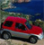 A red van with dark windows sits on a light-colored ground under a blue sky with green foliage in the background.