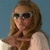 Pixelated image of a person with long brown hair wearing sunglasses and a light-colored top against a blue background.