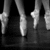 Black-and-white image of multiple dancers' feet in motion on a dark stage, with yellow text reading "Dancer For Life" on the right.