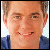 Pixelated close-up of a person with light brown hair, wearing a dark blue top, against a light background.