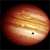 A pixelated spherical object with horizontal bands of orange, yellow, and brown hues against a black background, featuring a small dark square and a white dot on its surface.