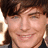 Pixelated close-up of a smiling person with brown hair and light skin, wearing a dark top against a blurred background.