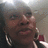 A pixelated close-up of a person with dark skin tone wearing large hoop earrings and holding a red rose, set against a blurred background.