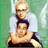 Two people in a pixelated image with green background; one person stands behind another, both wearing light shirts and dark pants.