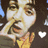 Pixelated close-up of a person with light skin and dark hair, hand near face, white heart symbol on dark background.