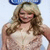 A pixelated image of a woman with long blonde hair wearing a white sleeveless top and blue headband, smiling against light background.