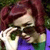 Pixelated image of a person with reddish-brown hair wearing a white top and blue-green garment, holding a green object near their face.