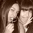 Two pixelated figures in sepia tones, one holding a small object near the other's face against a dark background.