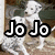 A white dog with dark eyes and nose stands on a brown surface against a blurred background, with text overlays changing across frames.