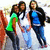 Three people pose together outdoors; the person on the left wears a green shirt, the middle person a white shirt, and the right person a blue shirt with a black jacket.