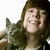 Pixelated image of a person with long brown hair wearing a dark jacket, holding a small dark animal against a white background.