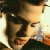 Pixelated close-up of a person with dark hair and light skin, wearing a dark shirt, against a bright background with warm tones.