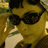 nine pixelated images showing a person with short dark hair in a brown top, transitioning from wearing sunglasses to removing them against a blurred background
