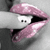 A close-up of lips with glossy pink lipstick, a finger touching the lips, and a small white object with two black dots inside the mouth.
