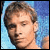 Pixelated static image of a person's face with brown hair against a blue background, rendered in low-resolution 256x256 pixels.
