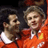 Two pixelated figures in orange sports uniforms with white accents, one holding a soccer ball, against dark background.